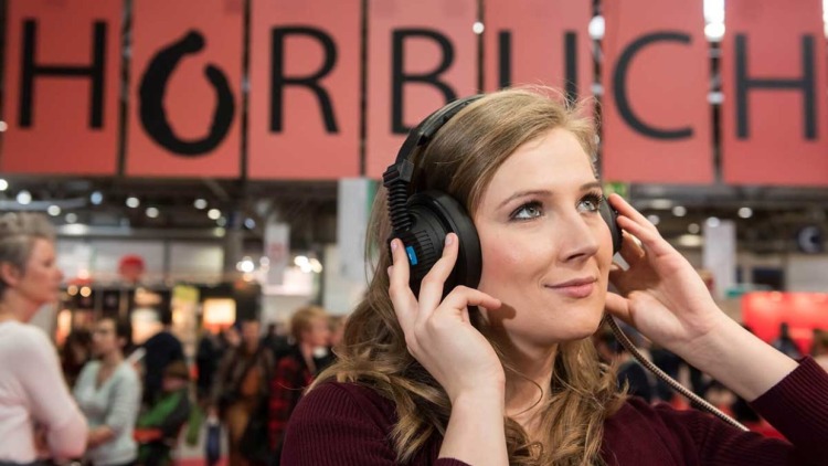 Junge Frau mit Kopfhörer auf der Leipziger Buchmesse vor einem großen Schild mit der Aufschrift "Hörbuch"